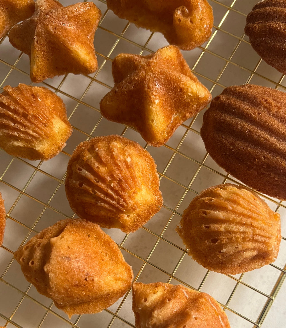 Star-shaped and seashell madeleines on a gold cooling rack.
